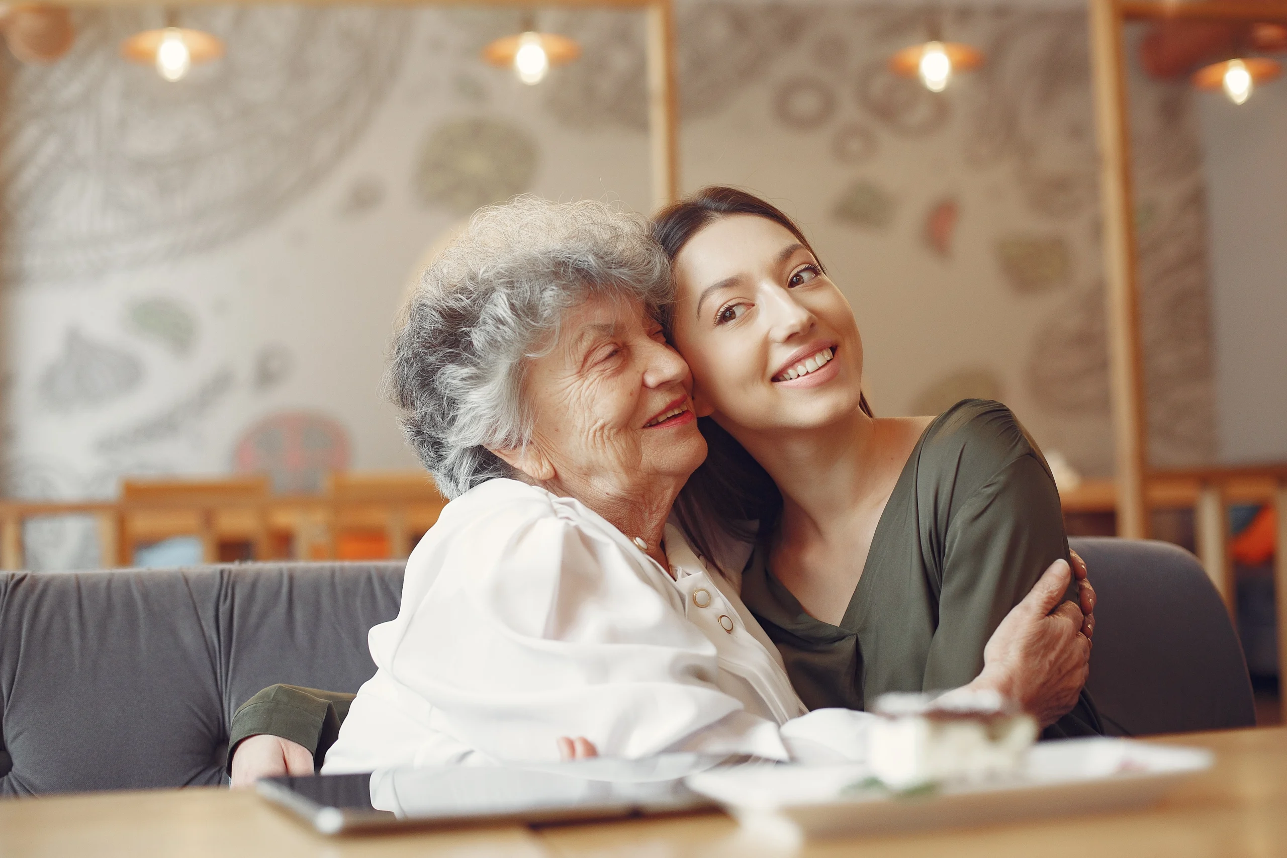 senior woman and female caregiver at dinner table share a hug and asmile