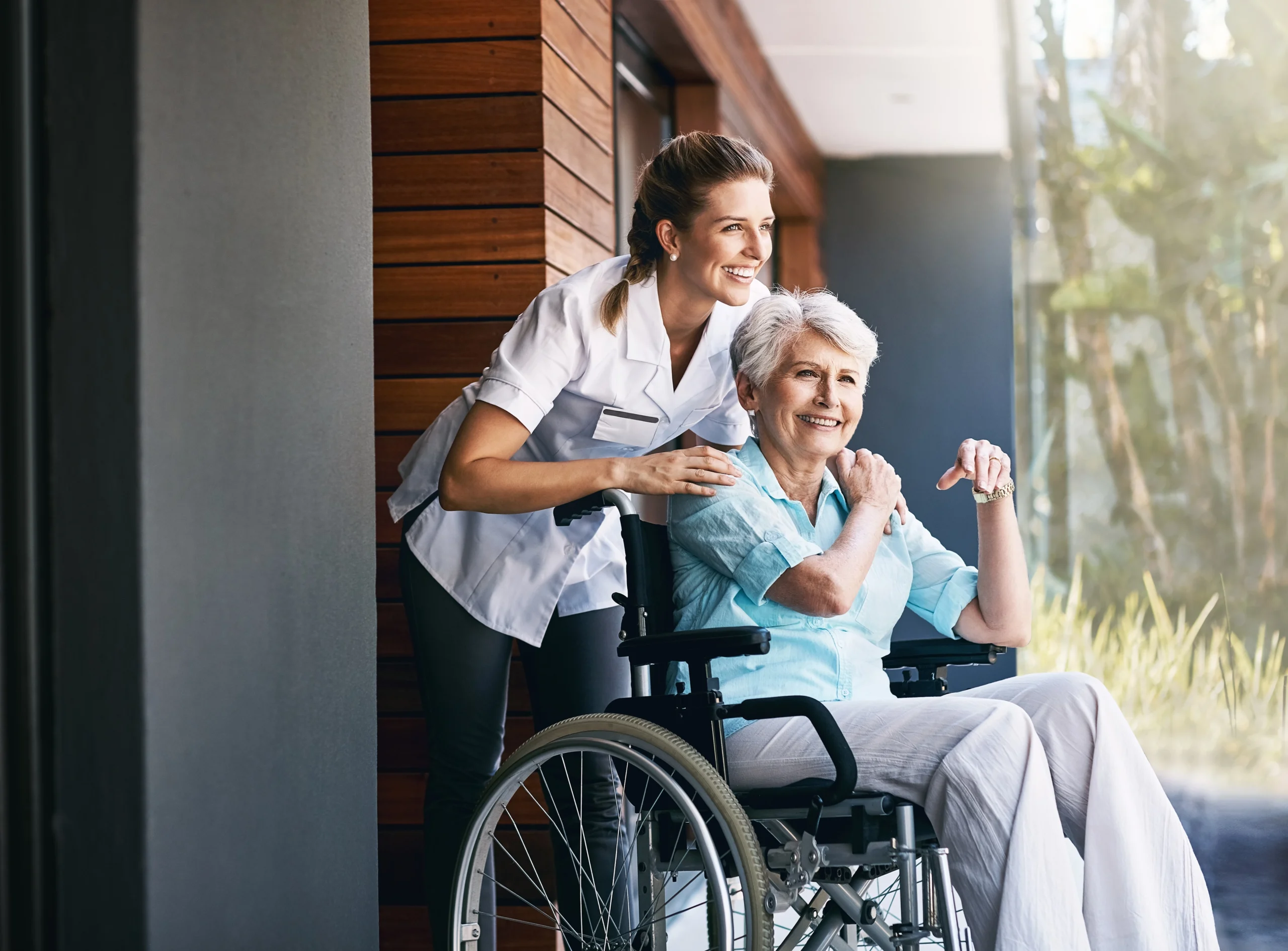 young smiling nurse pushes elderly woman in wheelchair for outdoor time