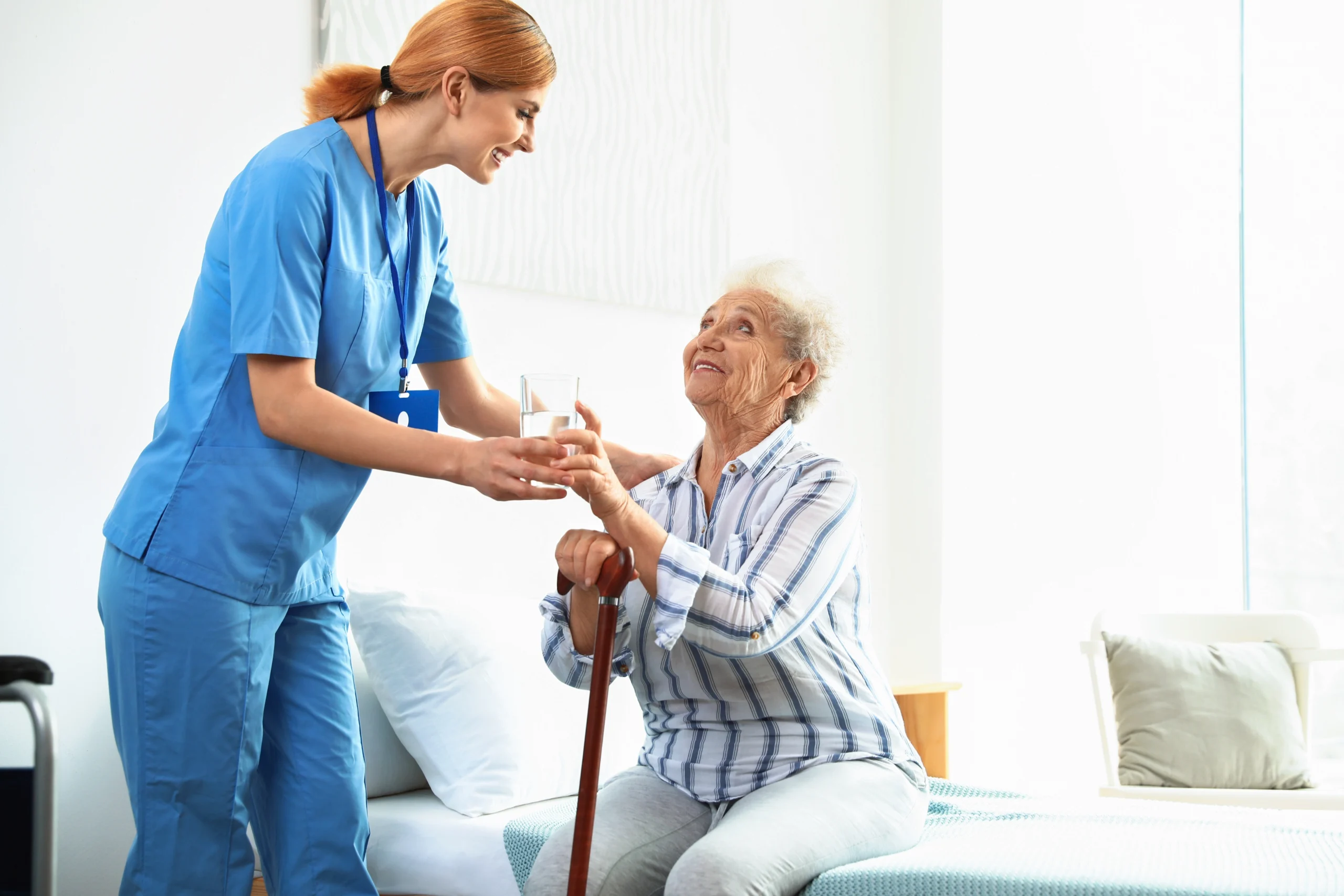 red-haired nurse hands a glass of water to aged woman