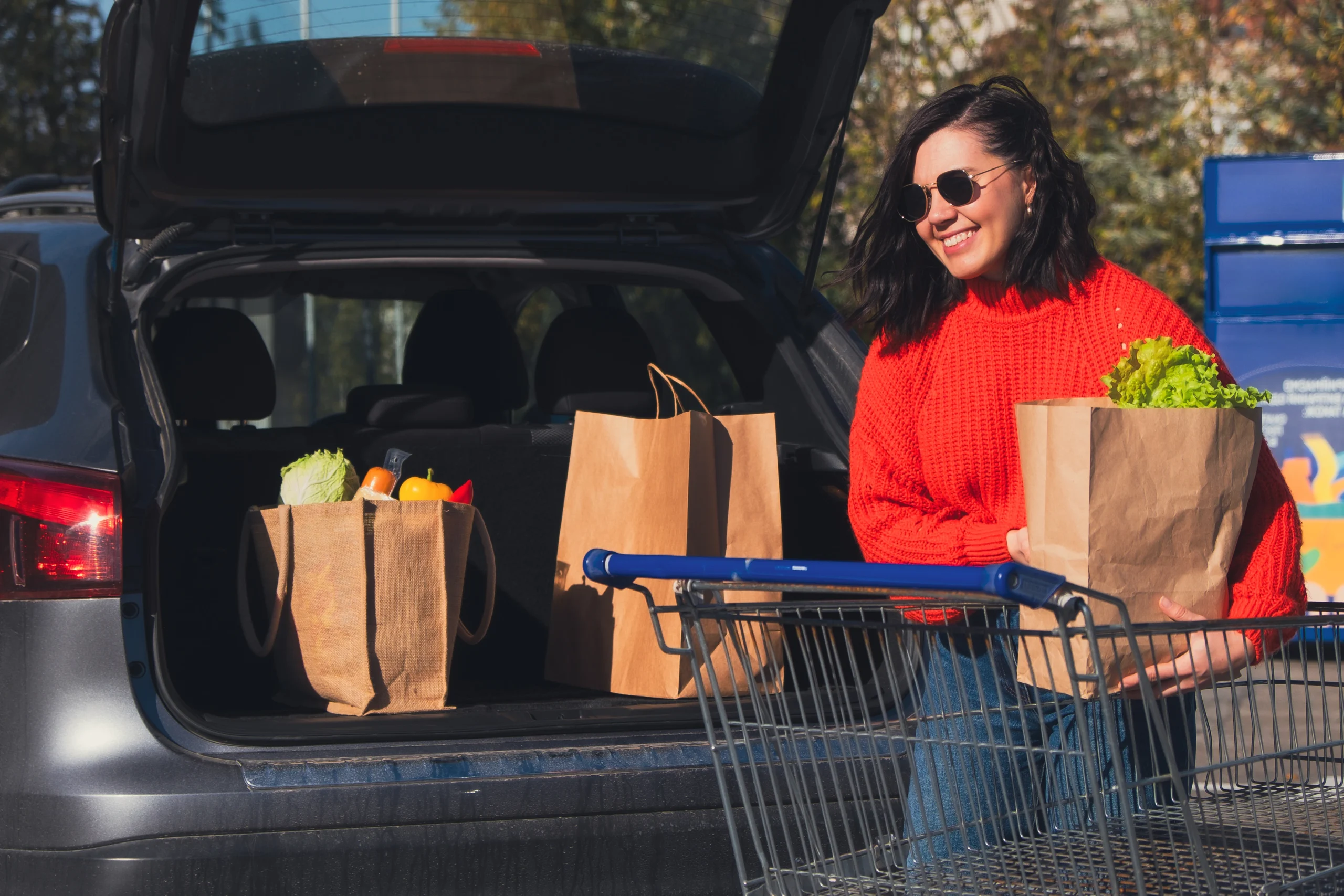 woman with red shirt taking grocery bags out of the trunk of her car