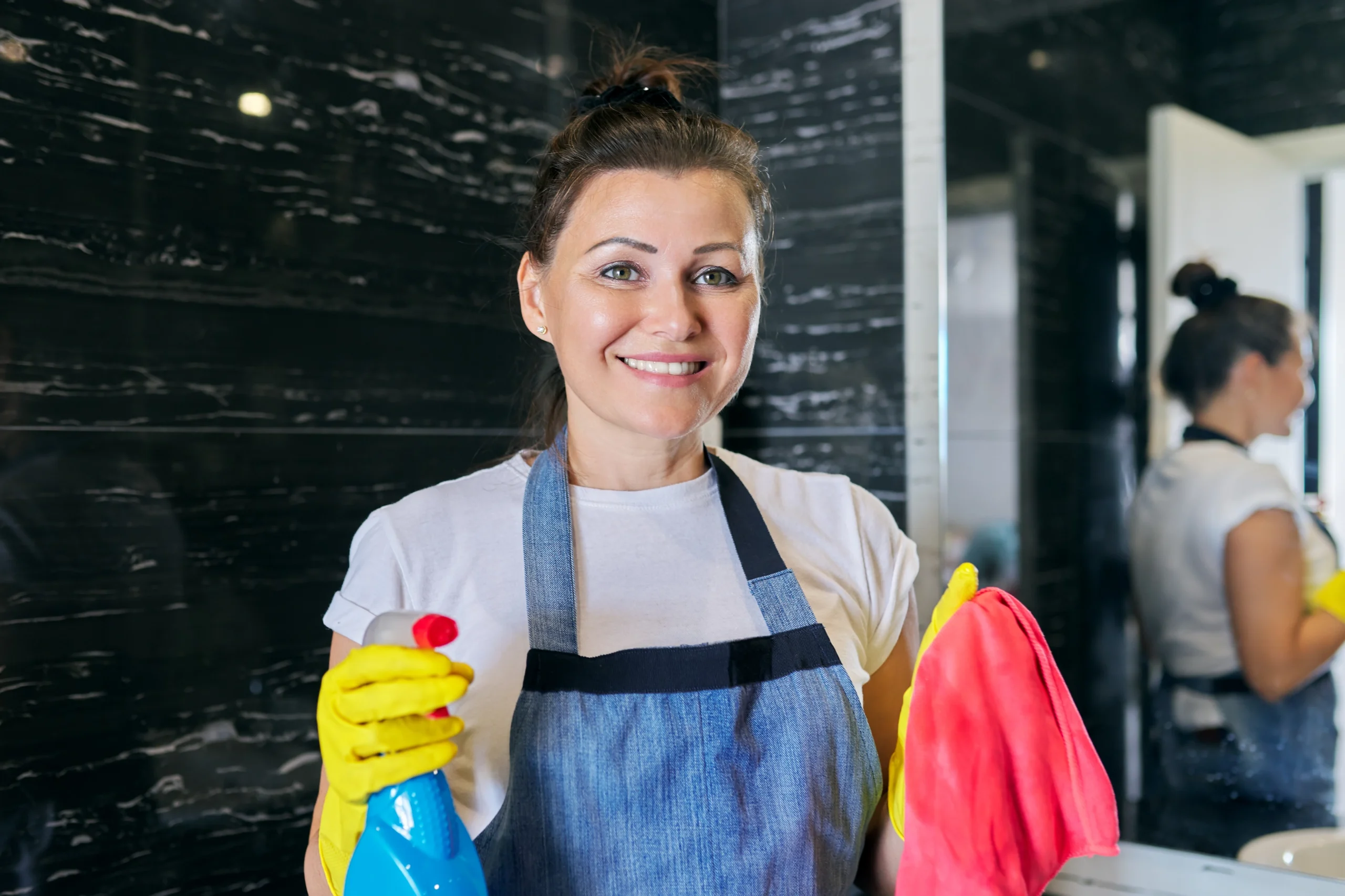 kousekeeper smiles with cleaning supplies in hand