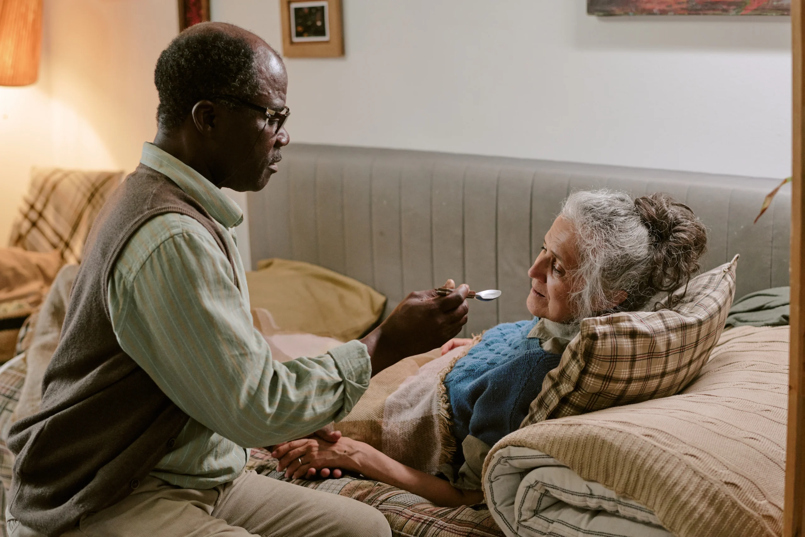 older caregiver feeds elderly woman on bedrest