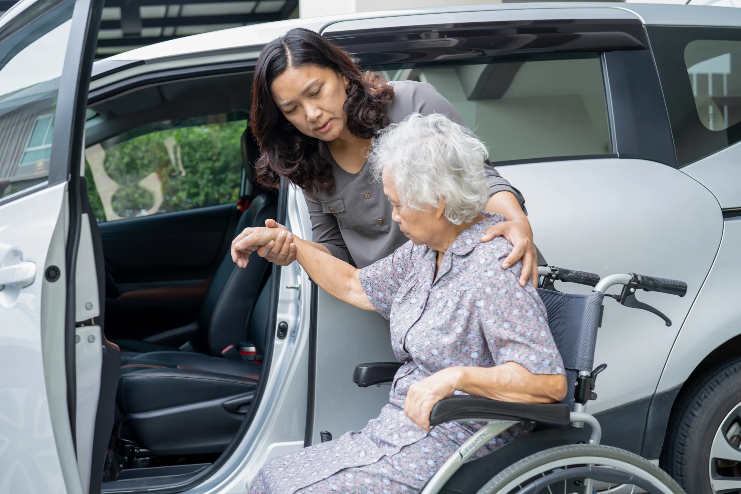 asian lady helps her grandmother get out of a wheelchair and into a van